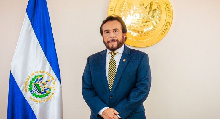 A photo of Felix Ulloa hijo standing next to the El Salvador national flag
